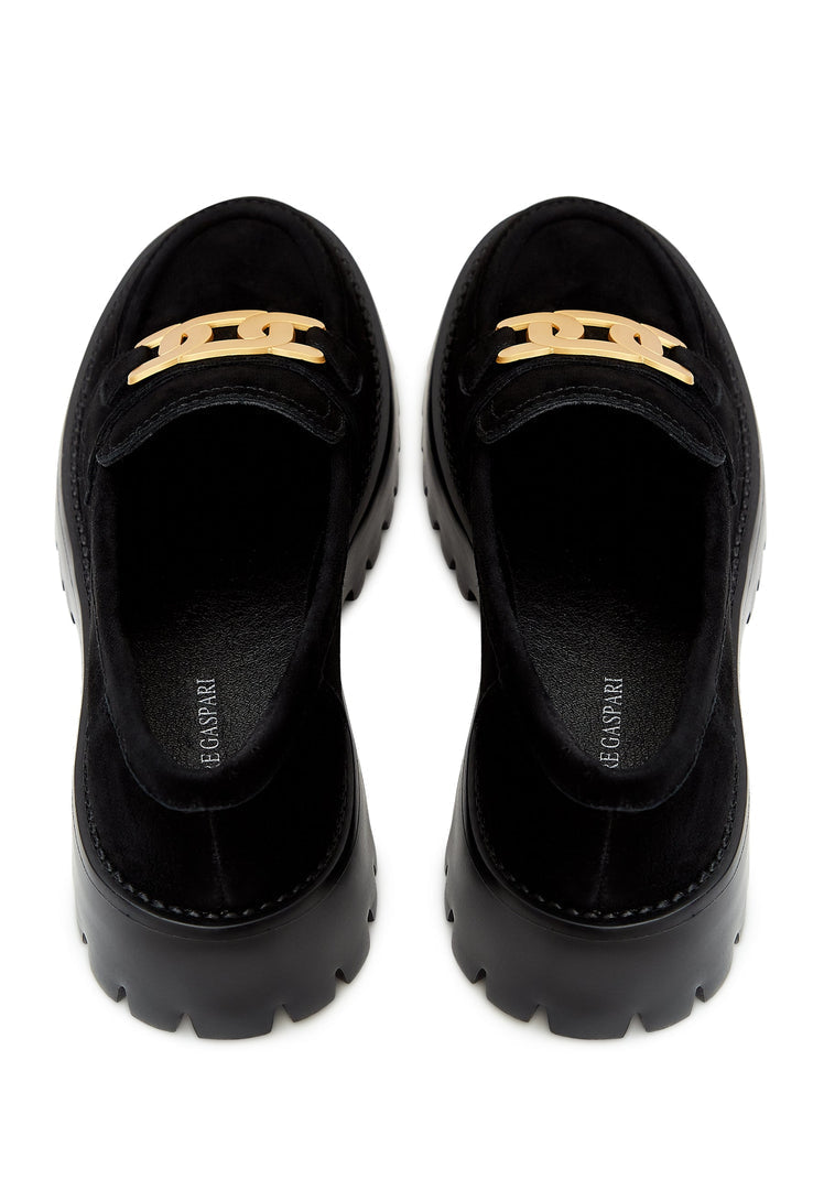 A fashionable pair of chunky black loafers with a golden chain detail, crafted from suede material, showcasing stylish footwear.