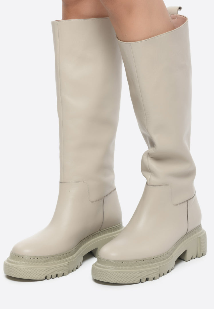 A fashionable pair of women's tall leather boots with a chunky sole in a stylish beige color, the perfect fashion footwear for any outfit.