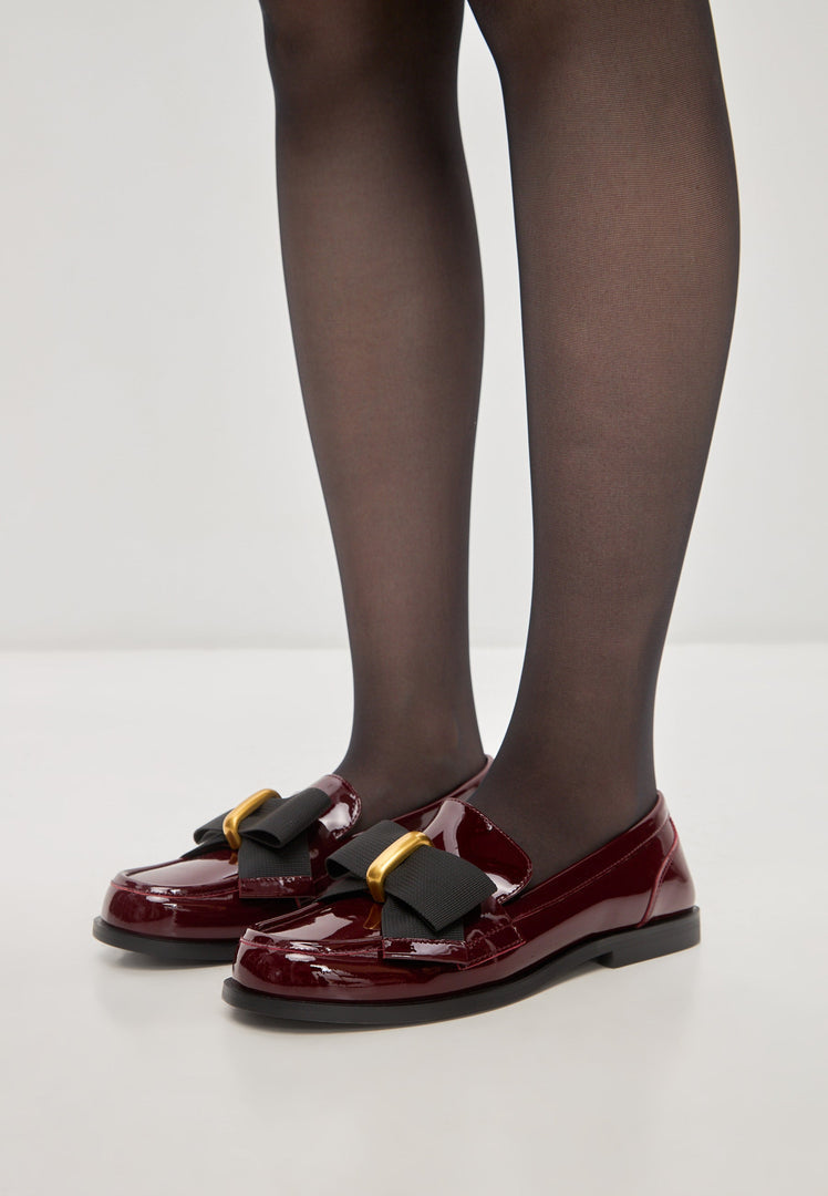 A pair of elegant loafers with black bow detail, also known as Dorothy loafers, featuring a patent red finish, perfect as women's dress shoes.