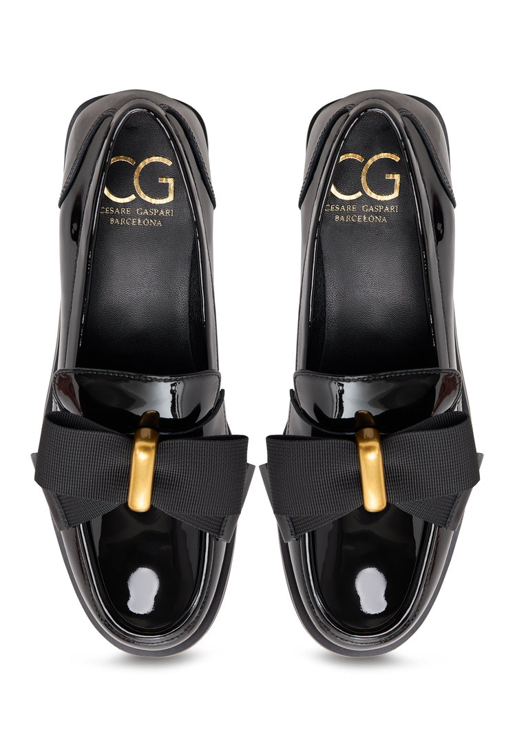 A pair of elegant patent black women's shoes with a gold bow detail, inspired by Dorothy's iconic style.