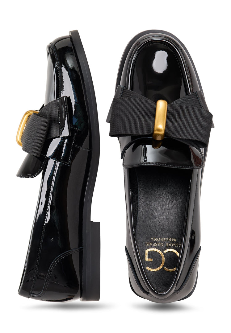 A pair of elegant patent black women's loafers with a gold bow inspired by Dorothy's iconic style.