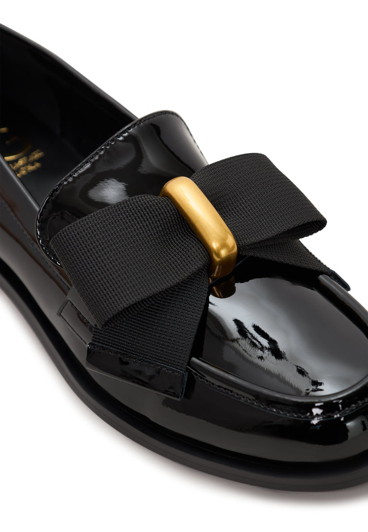 A pair of elegant loafers for women in patent black with a gold bow detail, inspired by Dorothy's iconic style.