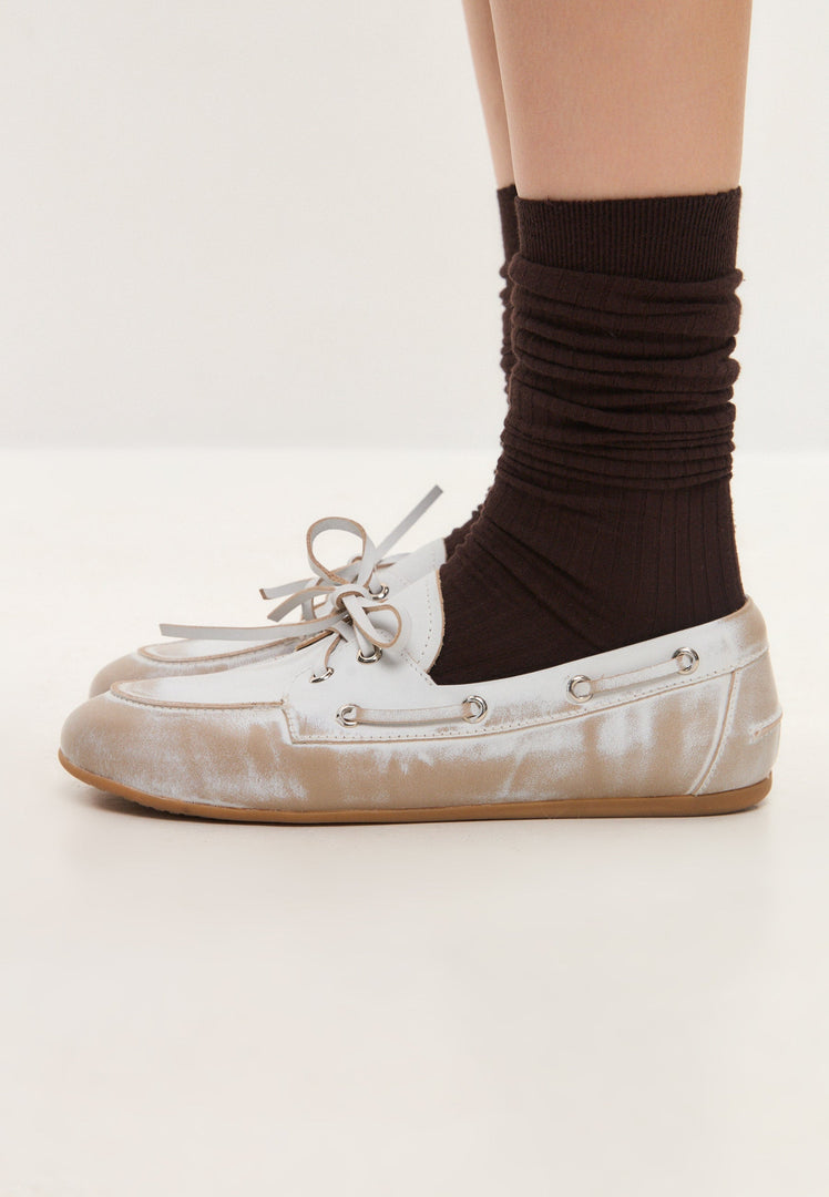 A pair of vintage leather loafers in distressed white, showcasing classic style and a worn-effect finish reminiscent of antique footwear.