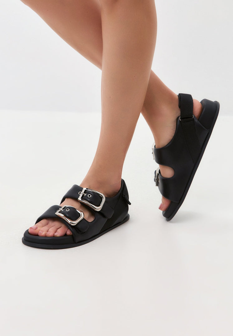A stylish pair of black wedge sandals with bold buckle detail, perfect for any woman looking to make a fashion statement with her shoes.