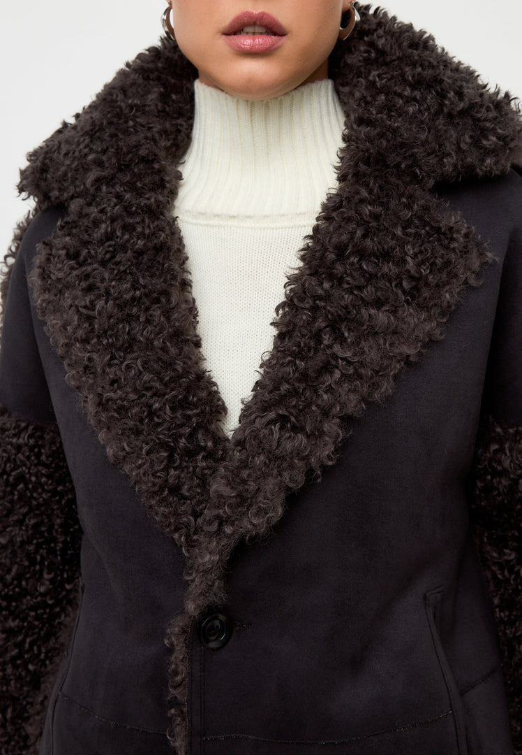 A stylish woman wearing a cozy shearling Eva coat in a classic black and brown color combination.