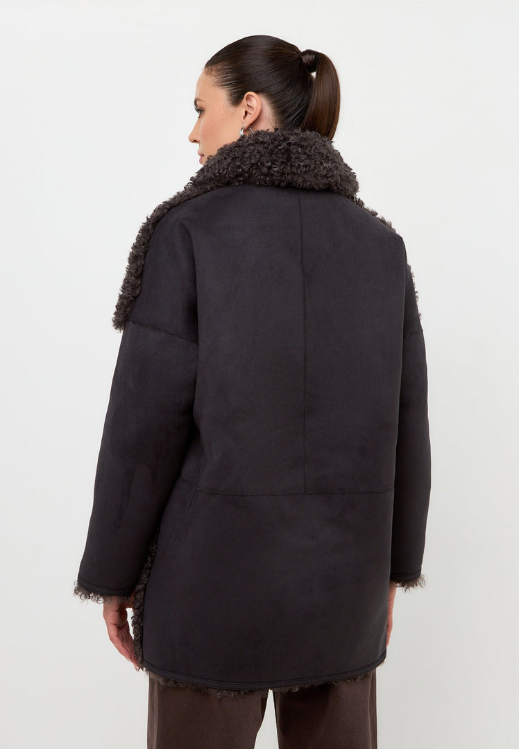 A fashionable woman wearing a cozy black shearling Eva coat, perfect for staying warm in cold weather.