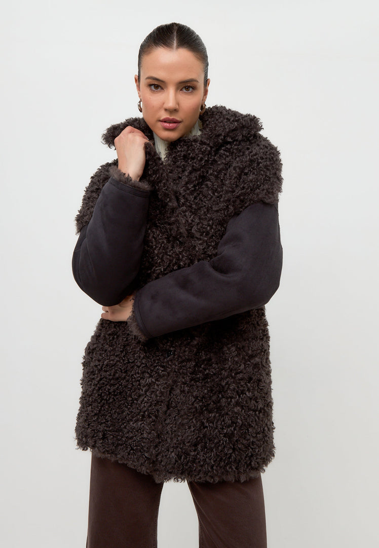 A stylish woman wearing a cozy black shearling Eva coat, perfect for staying warm in the winter.