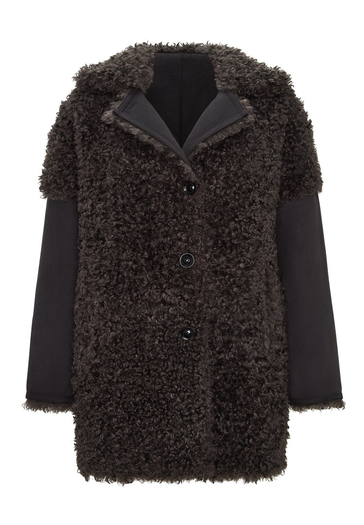A stylish woman wearing a cozy black shearling Eva coat with a luxurious brown lining.