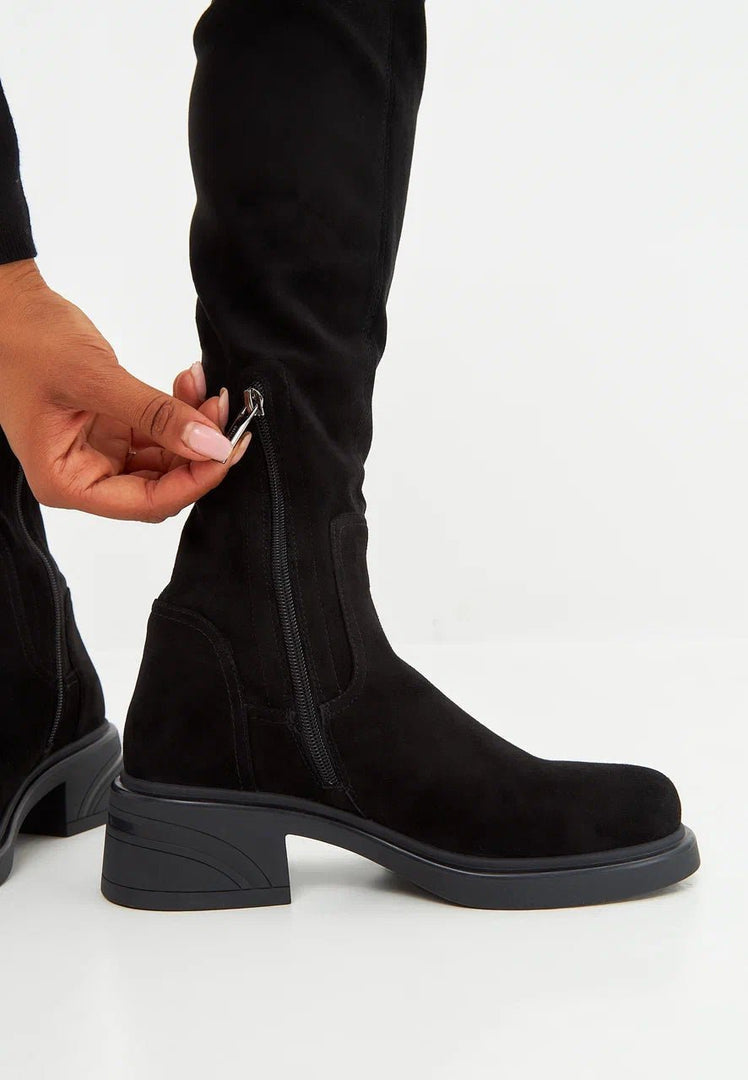 A fashionable woman wearing chic over-the-knee suede boots, a trendy choice in women's footwear for a stylish look.