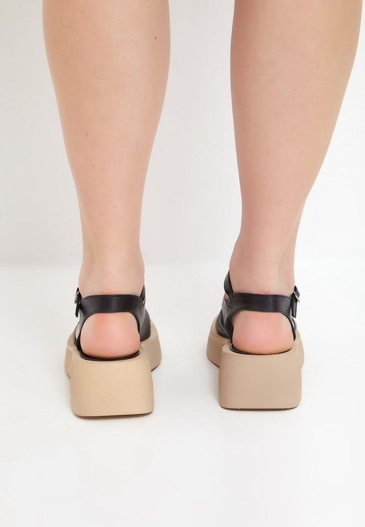 A woman's feet wearing stylish black platform sandals, the perfect mix of casual and comfortable footwear for any occasion.
