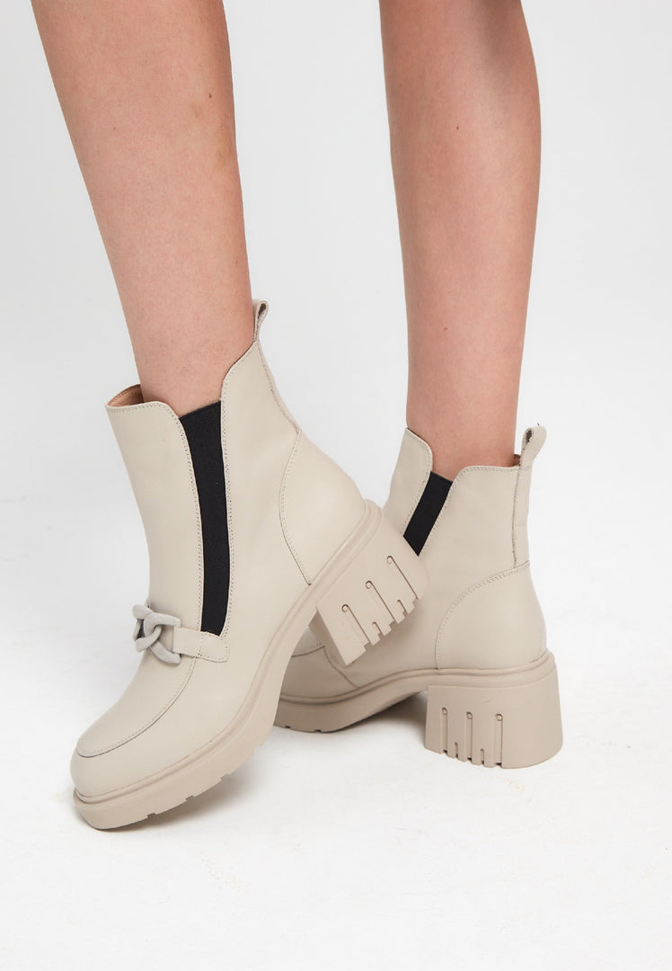 A stylish pair of beige chunky heel ankle boots with chain detail, perfect for women looking for fashionable footwear.