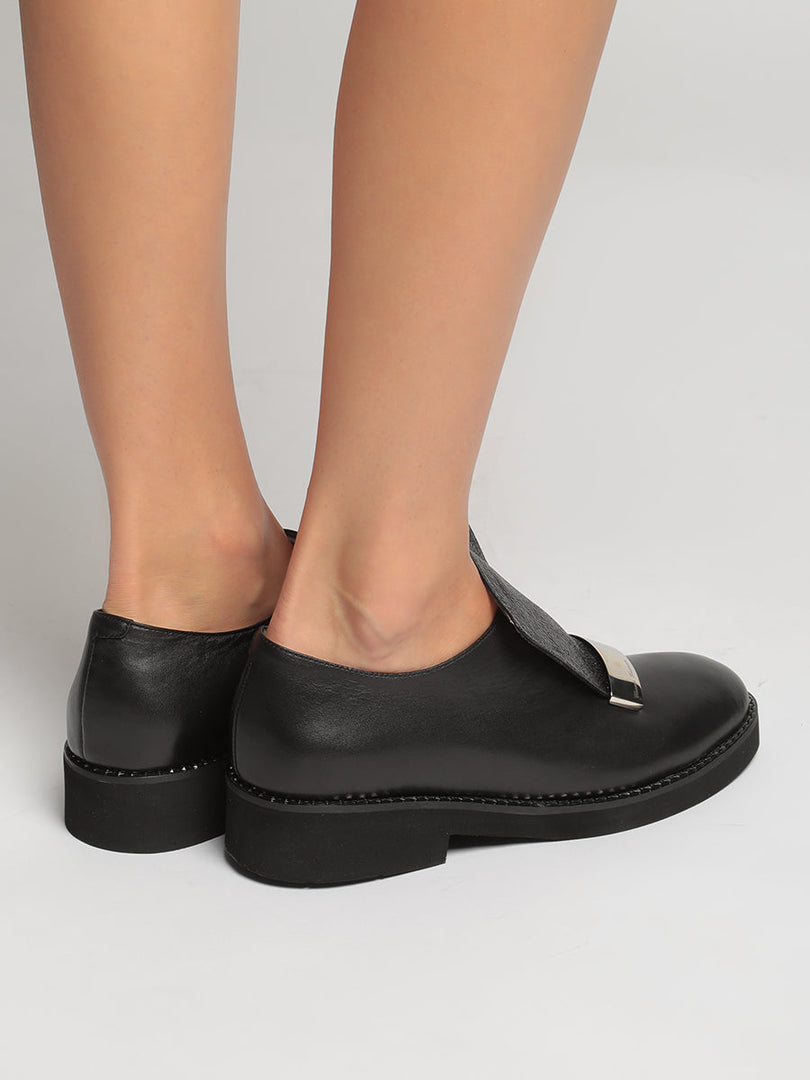 A trendy pair of men's leather slip-on loafers with a stylish metal accent, perfect for a fashionable and sophisticated look.