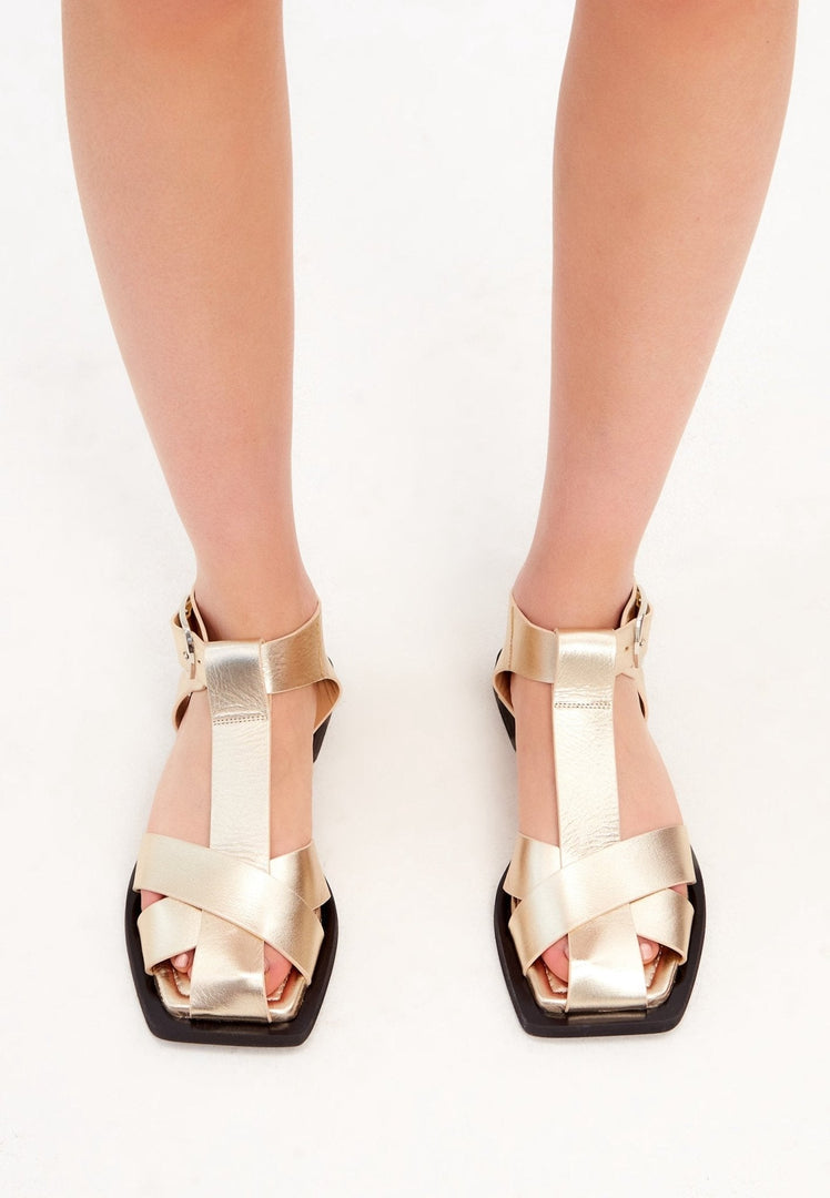 A close-up image of a pair of stylish gold ankle cuff sandals with a flat sole, perfect for women's summer footwear.