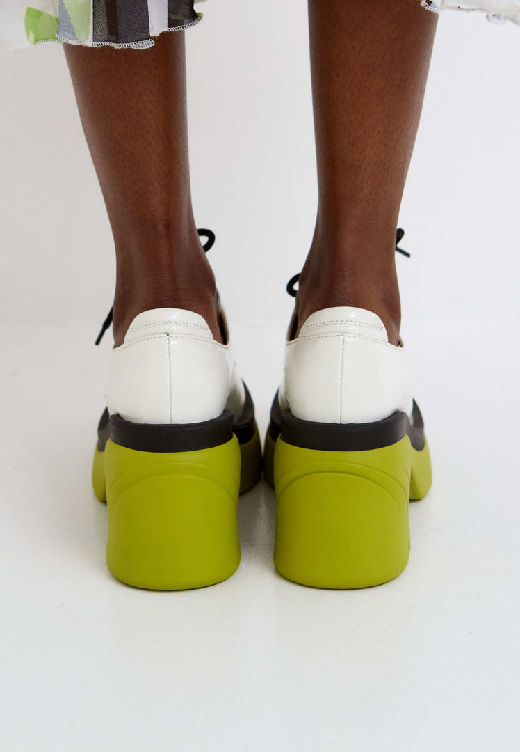 A trendy pair of white lace-up oxfords with chunky block heels, making a bold statement in women's fashion.