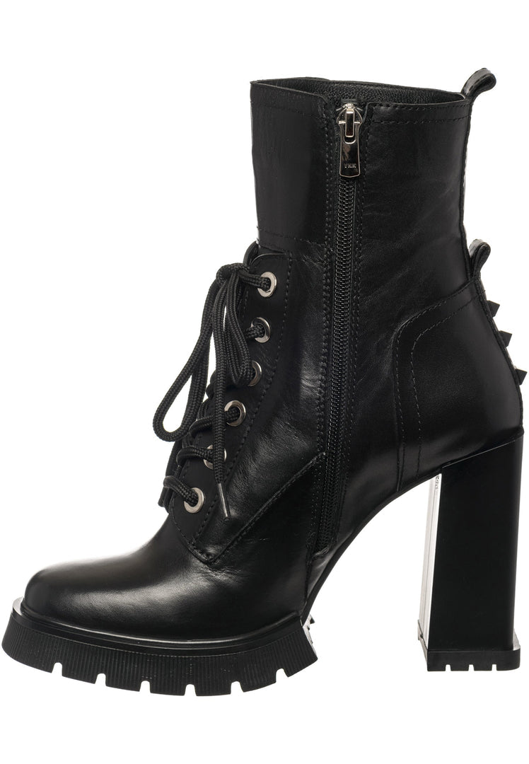 A woman standing crossed leg in a pair of fashionable heeled combat boots with edgy studs, perfect for women looking to add some attitude to their wardrobe.
