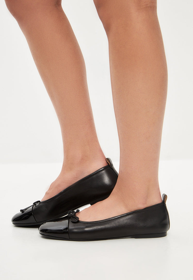 A stylish pair of black patent leather ballerinas known as Mila ballerinas, the perfect choice for women seeking chic and comfortable black patent flats.